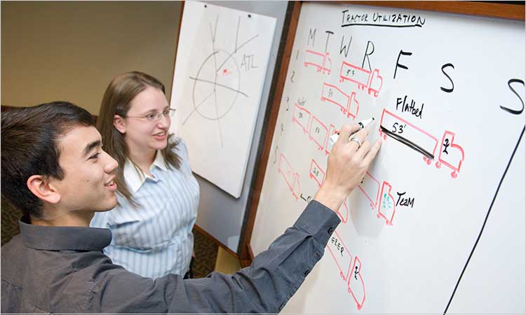 Photo of two students in front of whiteboard working on logistics issue BS IE Supply Chain Engineering Concentration