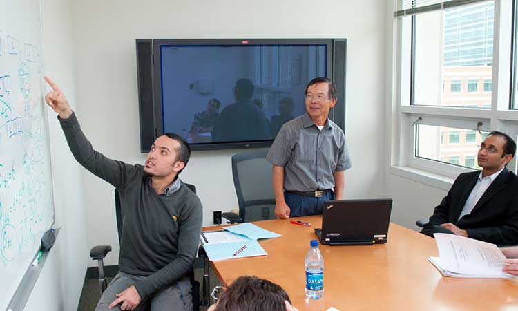 PhD student discussing research with faculty advisors in conference room.