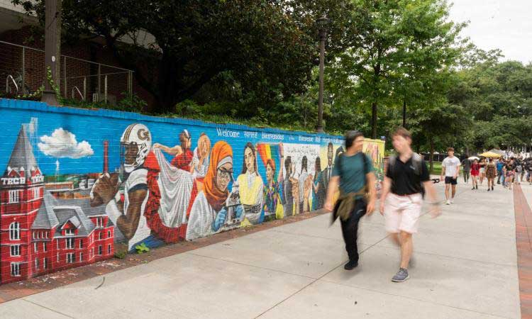 Two students walking on the GT campus alongside mural with GT elements